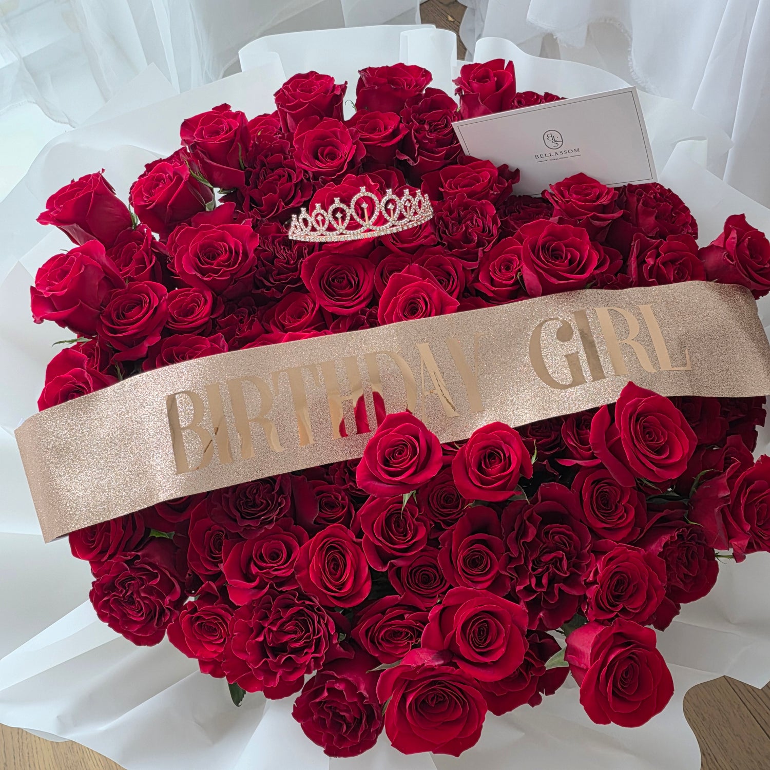 A "Birthday Queen" sash draped over a fabric-wrapped 100-rose box with a crown.