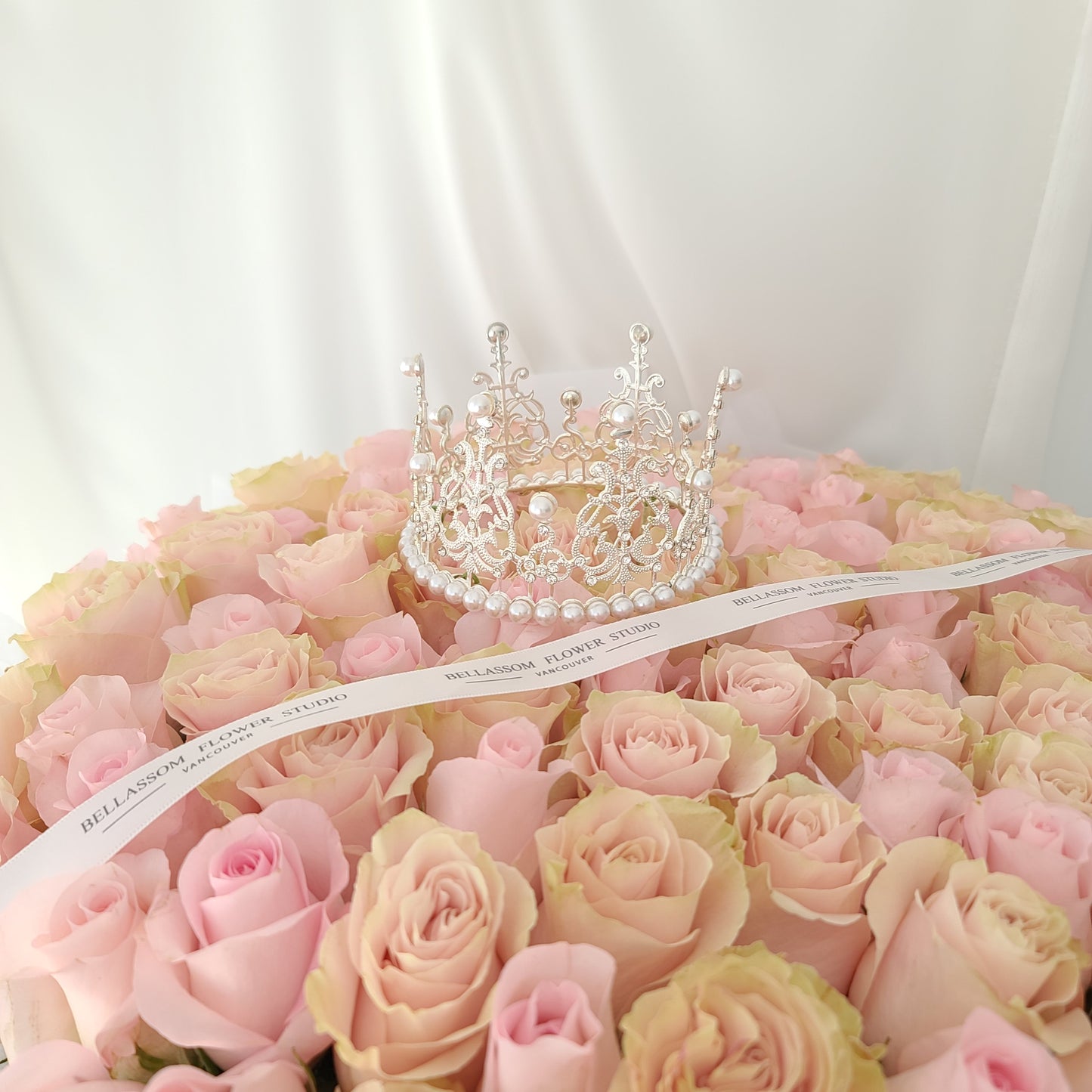 Close-up of premium pink roses with a sparkling crystal tiara and Bellassom branded logo ribbon.